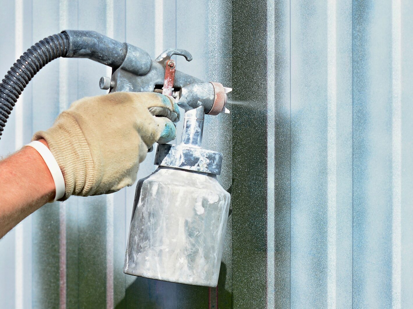 Spraying white paint onto a galvanized surface by an airbrush gun.